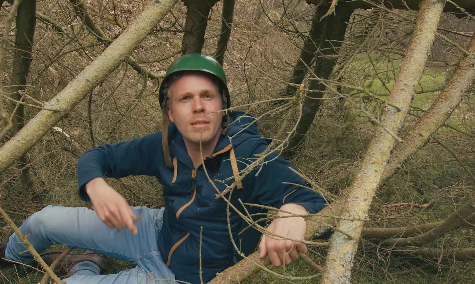 Ein Mann mit Kletterhelm sitzt zwischen abgebrochenen Ästen im Wald