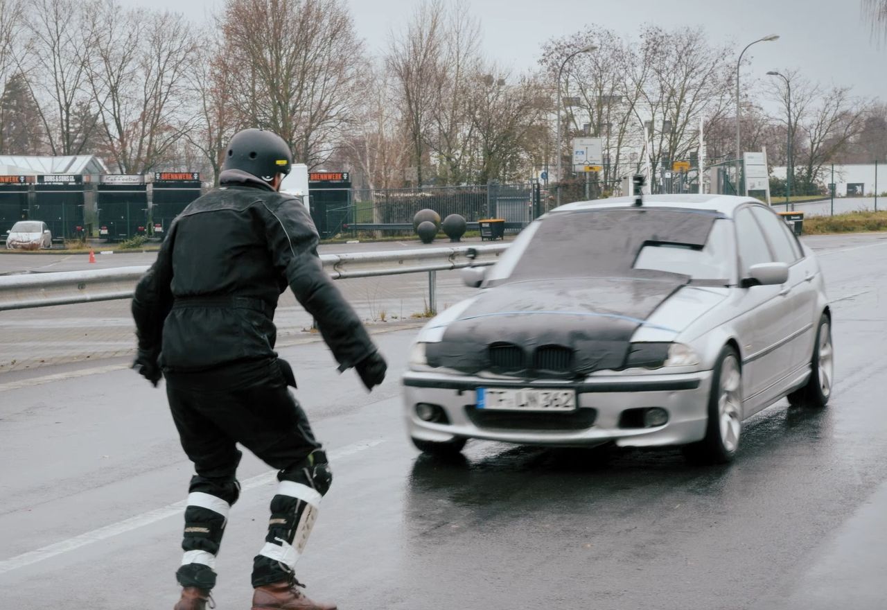 Ein Inline-Skater in Schutzausrüstung bremst vor einem Auto auf nasser Straße