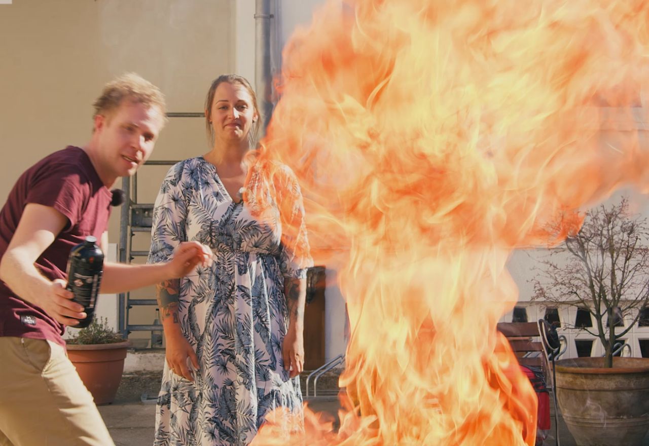 Zwei Menschen auf einer Terrasse weichen einer Feuersäule aus