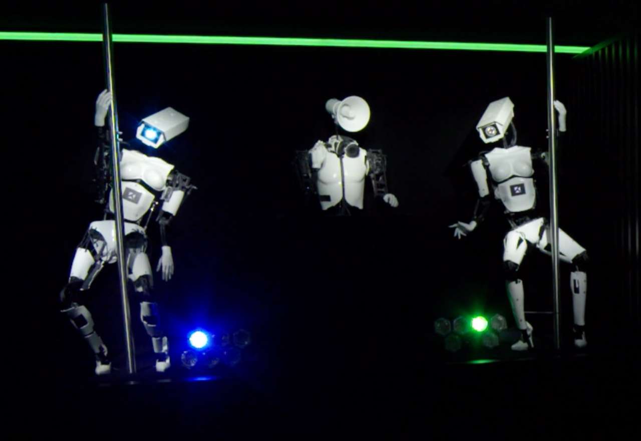 Drei humanoide Roboter an Stangen in einer dunklen Halle