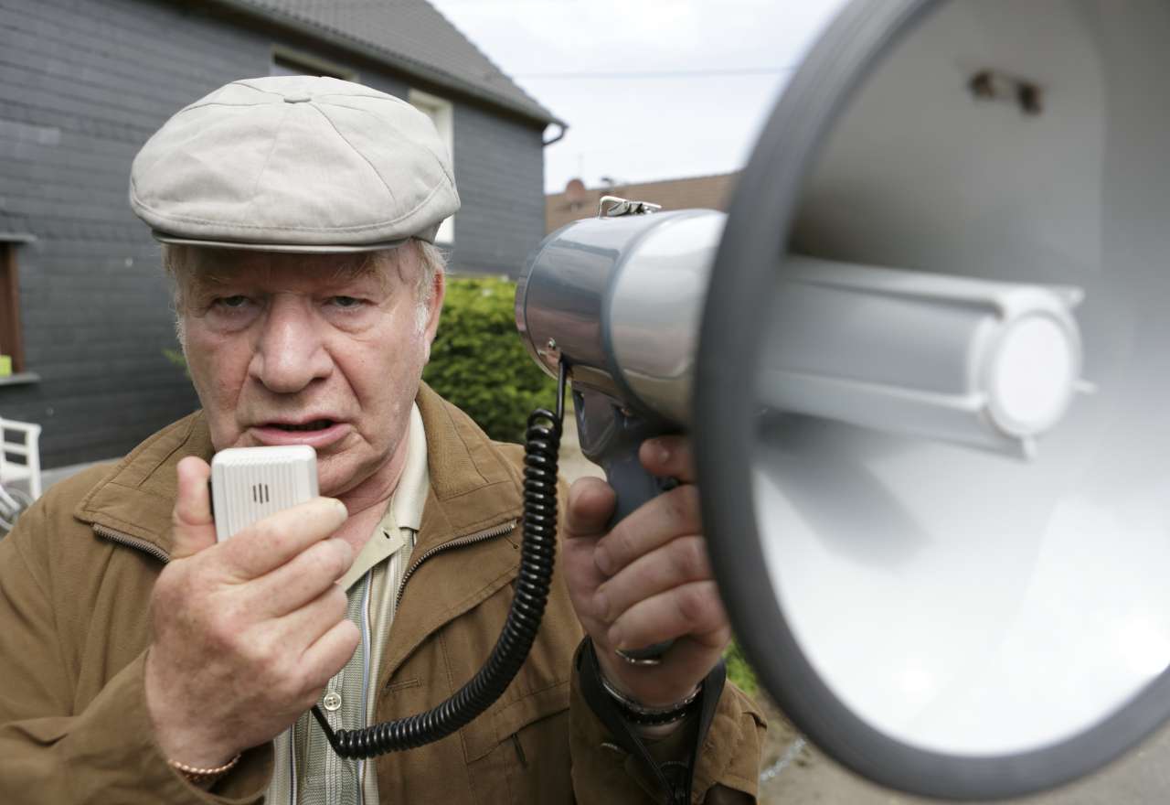 Ein älterer Mann mit Schiebermütze spricht in ein Megafon