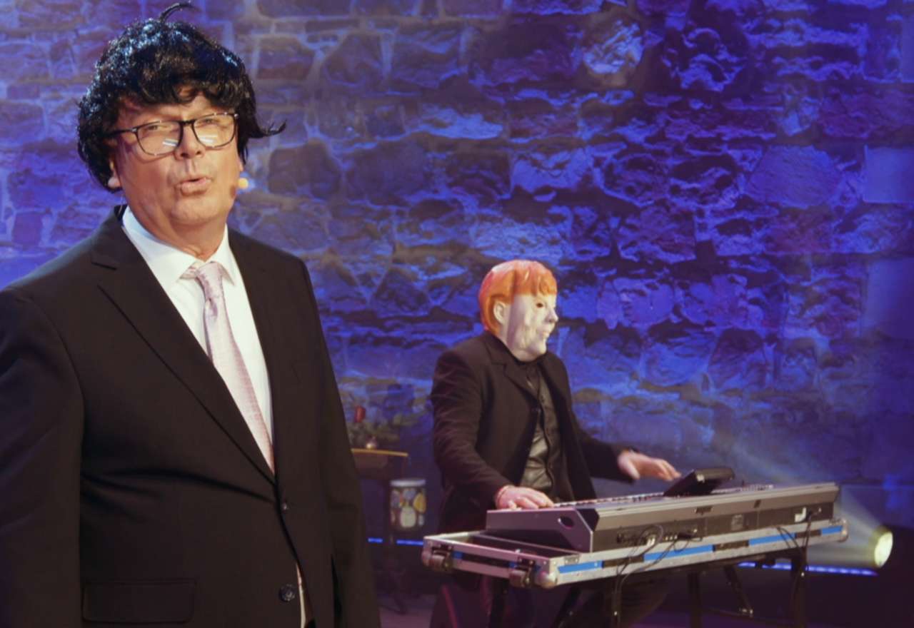 Zwei Bühnenfiguren mit Perücken, eine davon am Keyboard