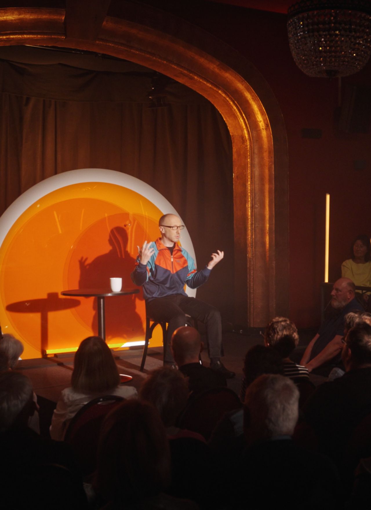 Blick über das Publikum auf die orange beleuchtete Bühne