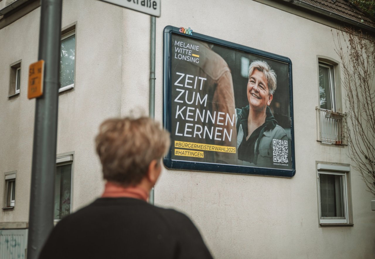 Eine Passantin betrachtet ein Wahlplakat an einer Hauswand